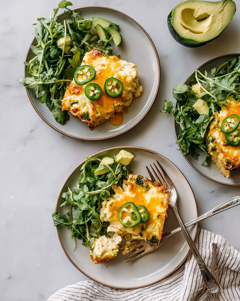 The image shows three white plates on a white marbled surface, each with a fresh salad of green leafy arugula and a half avocado sliced thinly on the top right. On each plate, there is one piece of cheesy casserole in the bottom center: the casserole has a golden-brown crust with melted yellow and white cheese dripping slightly and slices of green jalapeño scattered on top. The plate at the bottom also holds a fork partially inserted into the casserole, and a striped light-colored cloth is beneath it. The whole setting is bright and fresh. photo taken with an iphone --ar 4:5 --v 7