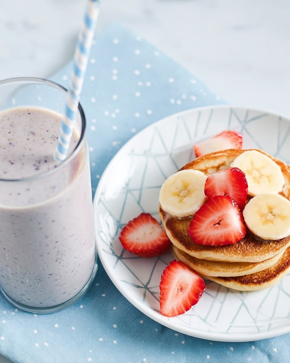 A close-up image of a tall clear glass filled with a light purple smoothie with tiny dark specks inside, with a pastel blue and white striped straw sticking out. To the left, a white plate with a single pancake topped with two slices of yellow banana and four bright red strawberry pieces, sitting on a light blue cloth with small white polka dots. The background is a white marbled surface. Photo taken with an iphone --ar 4:5 --v 7