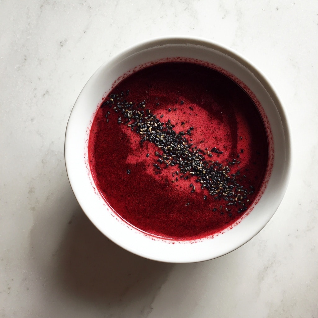 A round white bowl filled with a smooth, thick deep red beetroot soup. A line of small black seeds runs down the middle on top, adding a slight contrast. The bowl sits on a white marbled surface, highlighting the rich color of the soup. photo taken with an iphone --ar 4:5 --v 7
