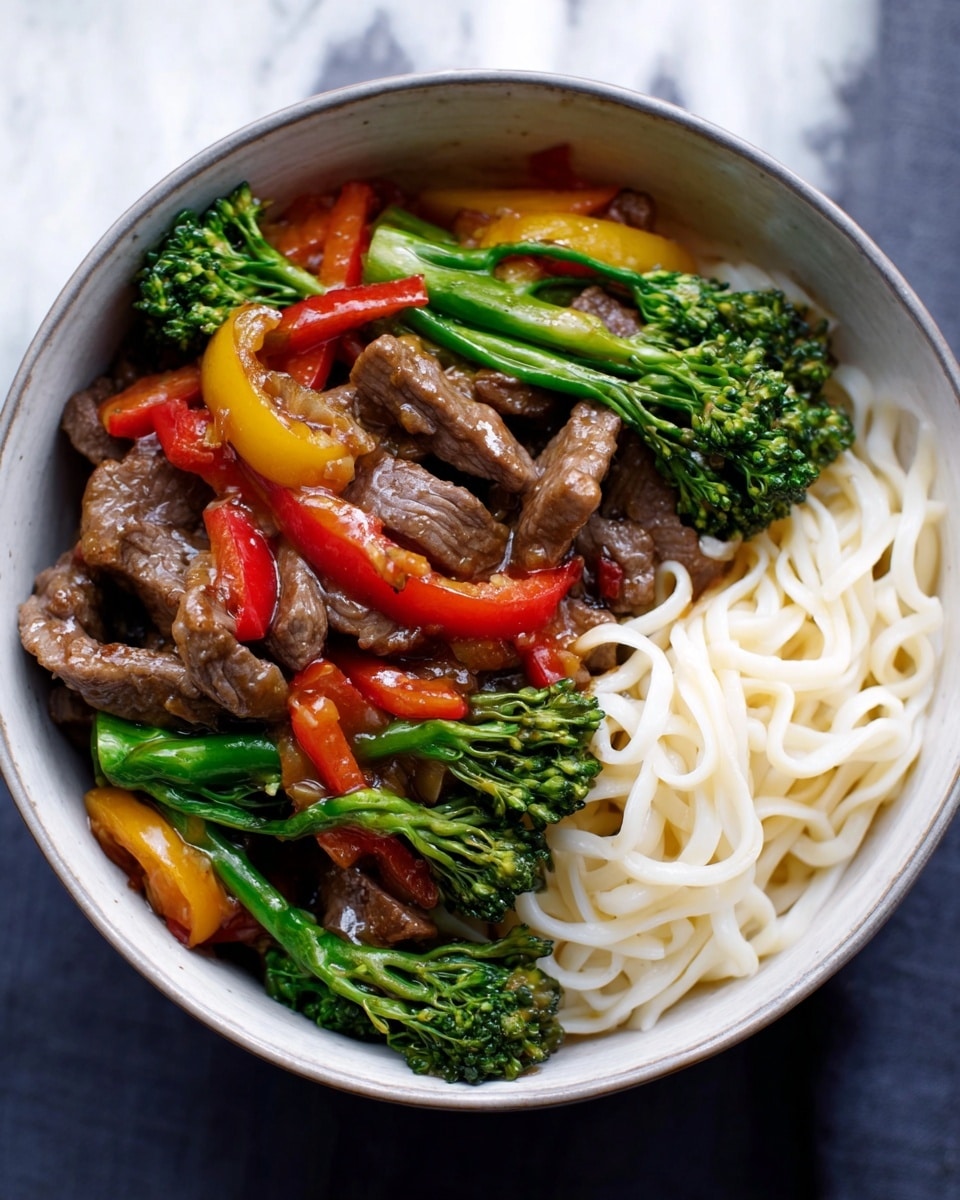 The image shows a bowl with two main layers: one side has soft, white noodles with a smooth texture, while the other side has a colorful mix of cooked beef slices that look tender, bright green broccolini with a fresh, slightly glossy surface, and pieces of red and yellow bell peppers that add vibrant color. The bowl is deep with a red inside and a black outside, placed on a white marbled surface. The ingredients look fresh and well-arranged, creating a balanced and inviting meal photo taken with an iphone --ar 4:5 --v 7