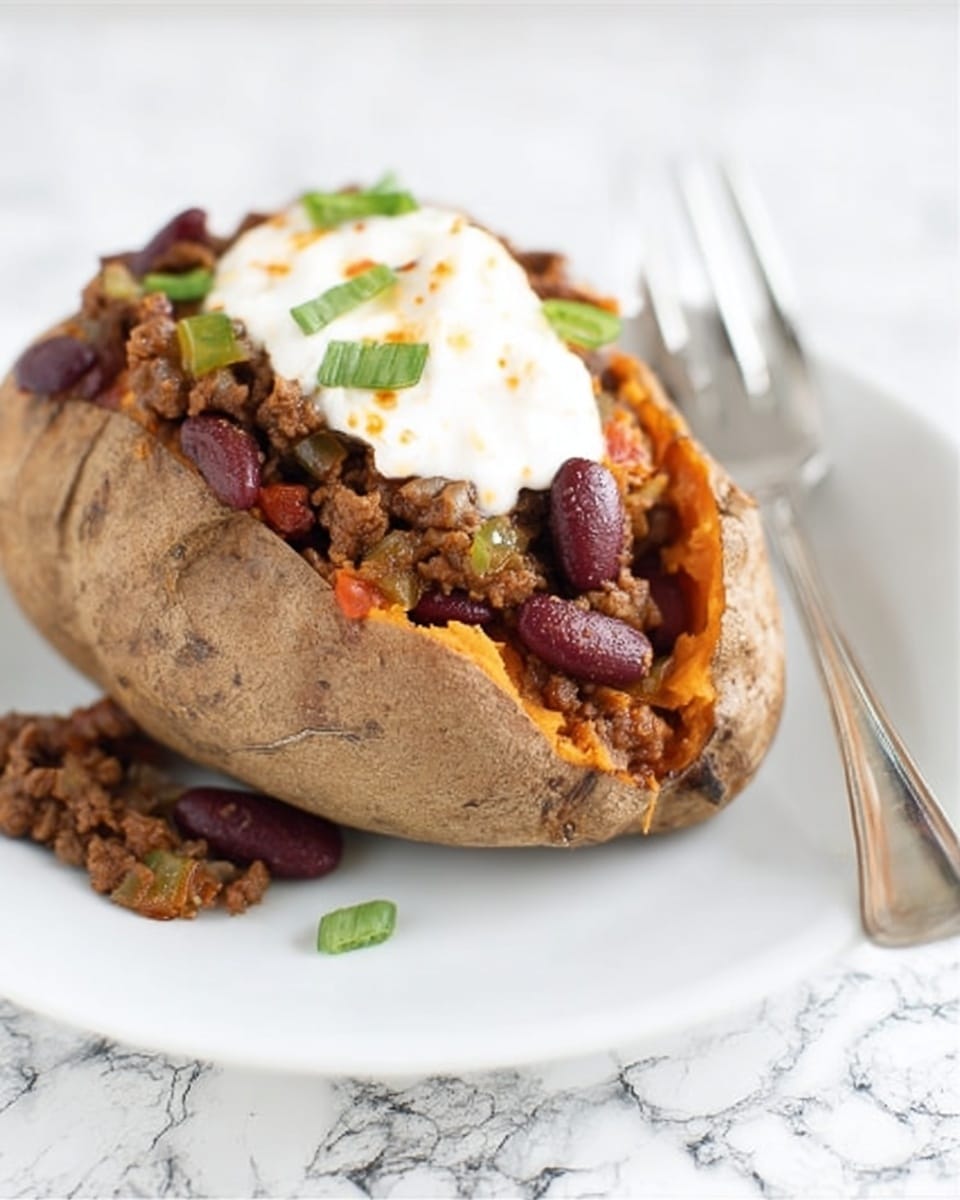 A baked sweet potato with a dark brown, rough skin is cut open and filled with a layer of cooked chili made of ground meat, red kidney beans, and small bits of green peppers. On top of the chili, there is a layer of white creamy sauce, slightly melting and spreading over the chili. This all sits on a plain white plate, with a silver fork placed next to the potato. The background is a white marbled surface. Photo taken with an iphone --ar 4:5 --v 7
