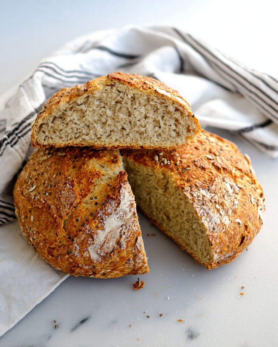 A round loaf of crusty bread, roughly broken into three large pieces with a golden-brown, textured crust showing seeds and grains. The inside is light beige with a dense, soft, and slightly crumbly texture. The bread rests on a white marbled surface next to a white cloth with black stripes. Photo taken with an iphone --ar 4:5 --v 7