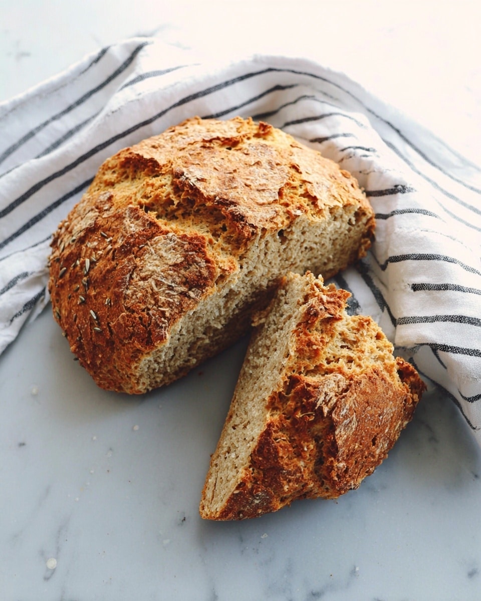 A round, golden-brown oat bread split into three large pieces resting directly on a smooth white marbled surface. The bread has a rough, crumbly texture with visible oats and a crunchy crust. One piece is leaning against the other two, showing the light beige, soft, and airy inside with small air pockets. A white cloth with black stripes lies loosely beside the bread. Photo taken with an iphone --ar 4:5 --v 7