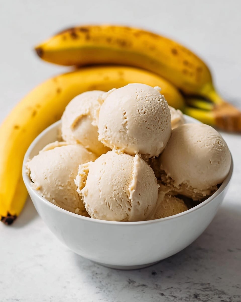 A white bowl filled with seven scoops of light beige ice cream, each scoop smooth with slight texture on top, stacked closely together inside the bowl. Two ripe yellow bananas rest leaning against the bowl on a white marbled surface in the background, creating a soft and bright setting. photo taken with an iphone --ar 4:5 --v 7