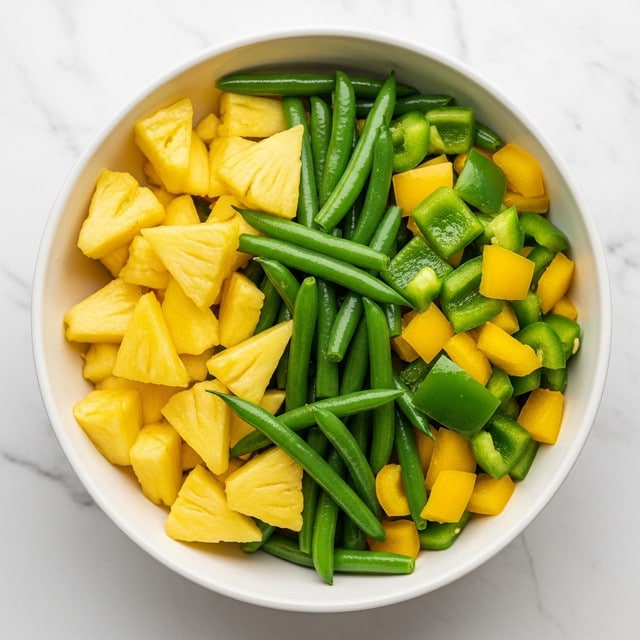 A white bowl filled with a colorful vegetable mix, including bright yellow pineapple chunks, green beans, and pieces of green and yellow bell peppers. The vegetables have a fresh, slightly shiny texture, and the bowl sits on a white marbled surface. The dish looks vibrant and healthy, with the pineapple pieces adding a soft, juicy contrast to the firmer beans and peppers. Photo taken with an iphone --ar 4:5 --v 7