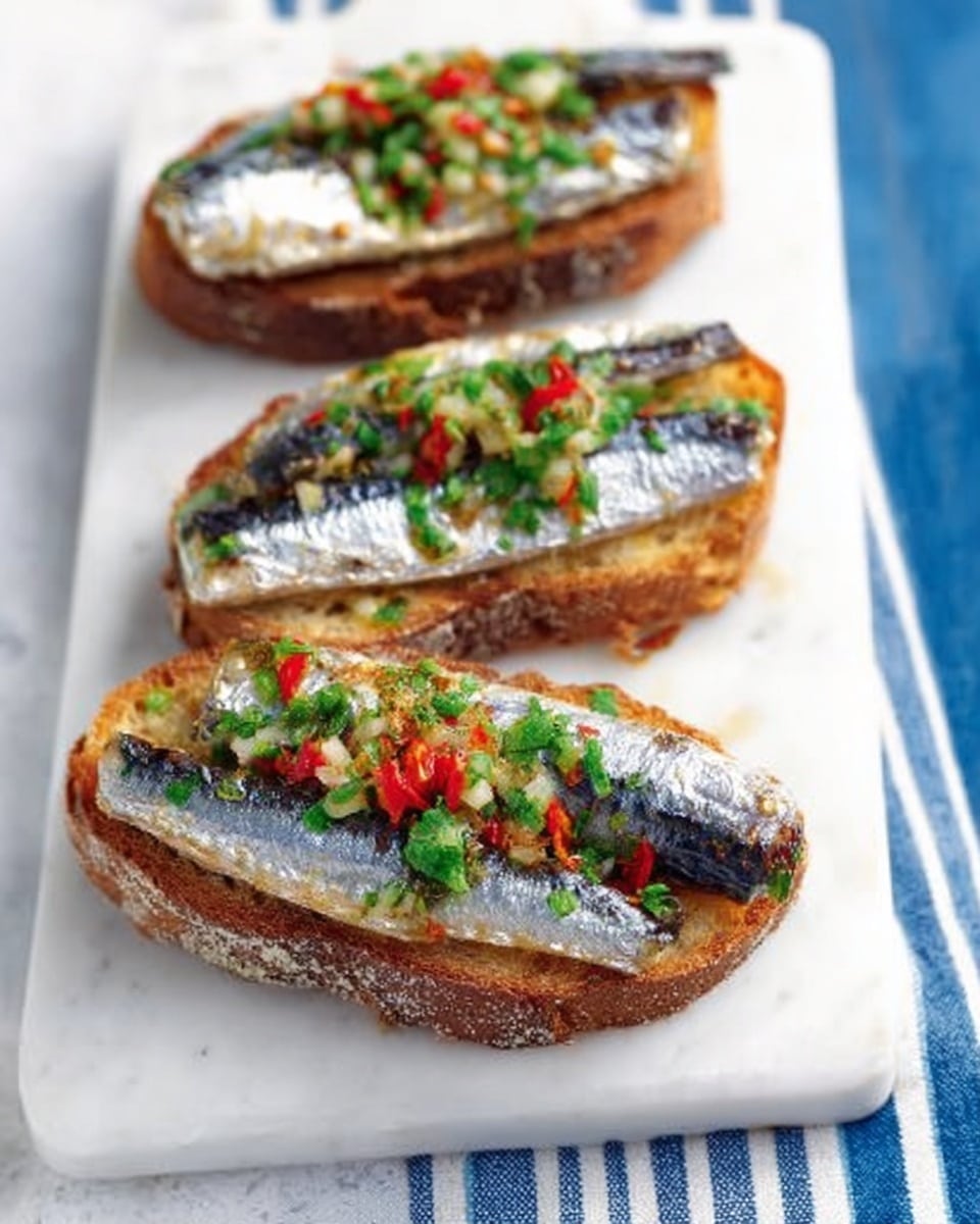 Two pieces of toasted bread are laid on a white marbled surface with a white cloth with blue stripes nearby. Each toast is topped with two silver sardines placed side by side, with their shiny, slightly oily skin visible. The sardines rest on a layer of green herbs and finely chopped red and yellow peppers, adding small bright pops of color. The bread has a dark, crispy crust and a coarse, rustic texture. Photo taken with an iphone --ar 4:5 --v 7
