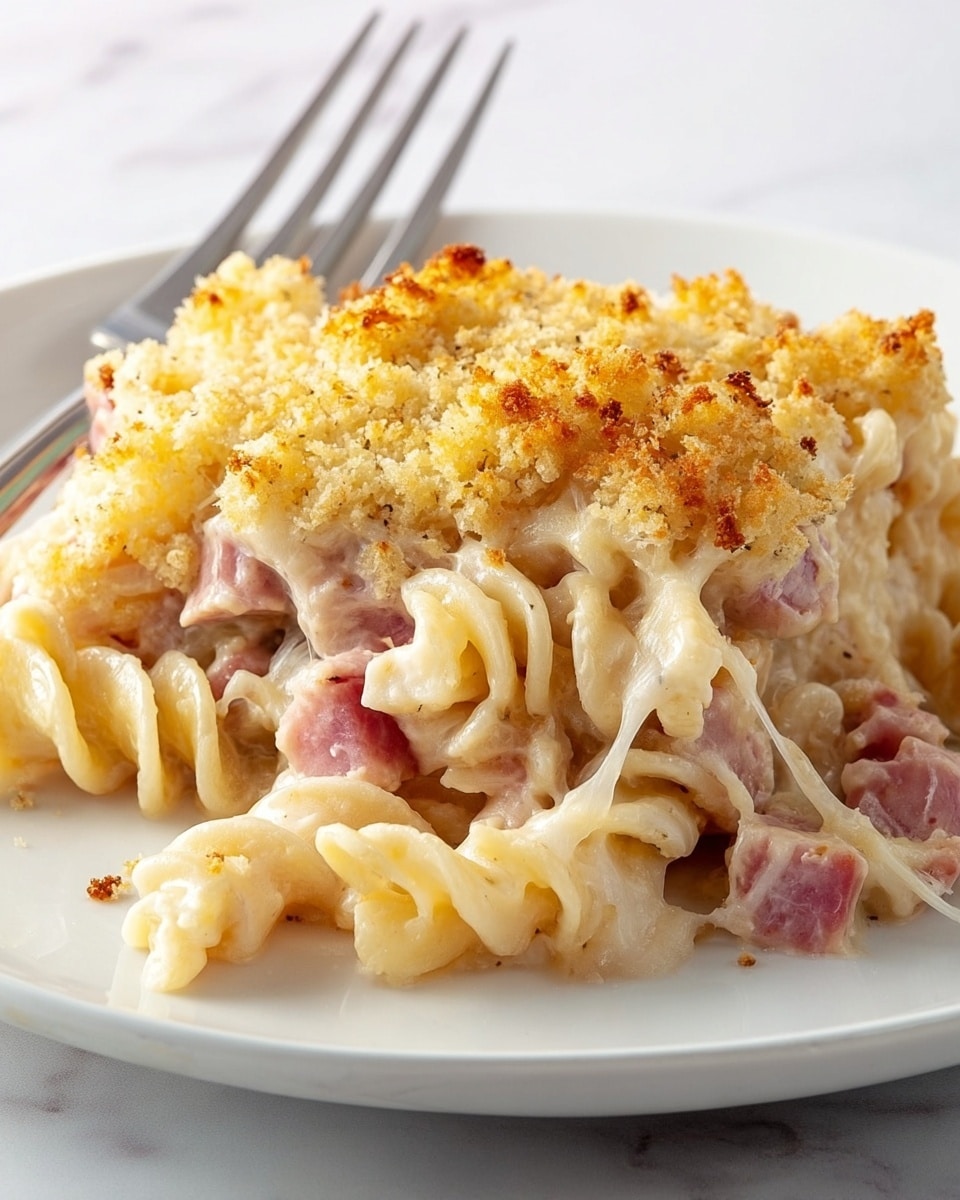 The dish is a creamy pasta bake served on a white plate with a fork resting on the edge. It has three visible layers: the bottom layer shows twisted pasta spirals coated in a smooth, creamy white sauce, scattered with chunks of pink ham. The middle layer has more pasta mixed with melted cheese that pulls slightly, creating thin cheese strings. The top layer consists of golden brown, crispy breadcrumbs that are unevenly spread and toasted to a light, crunchy texture with small darker spots. The plate sits on a white marbled surface. photo taken with an iphone --ar 4:5 --v 7