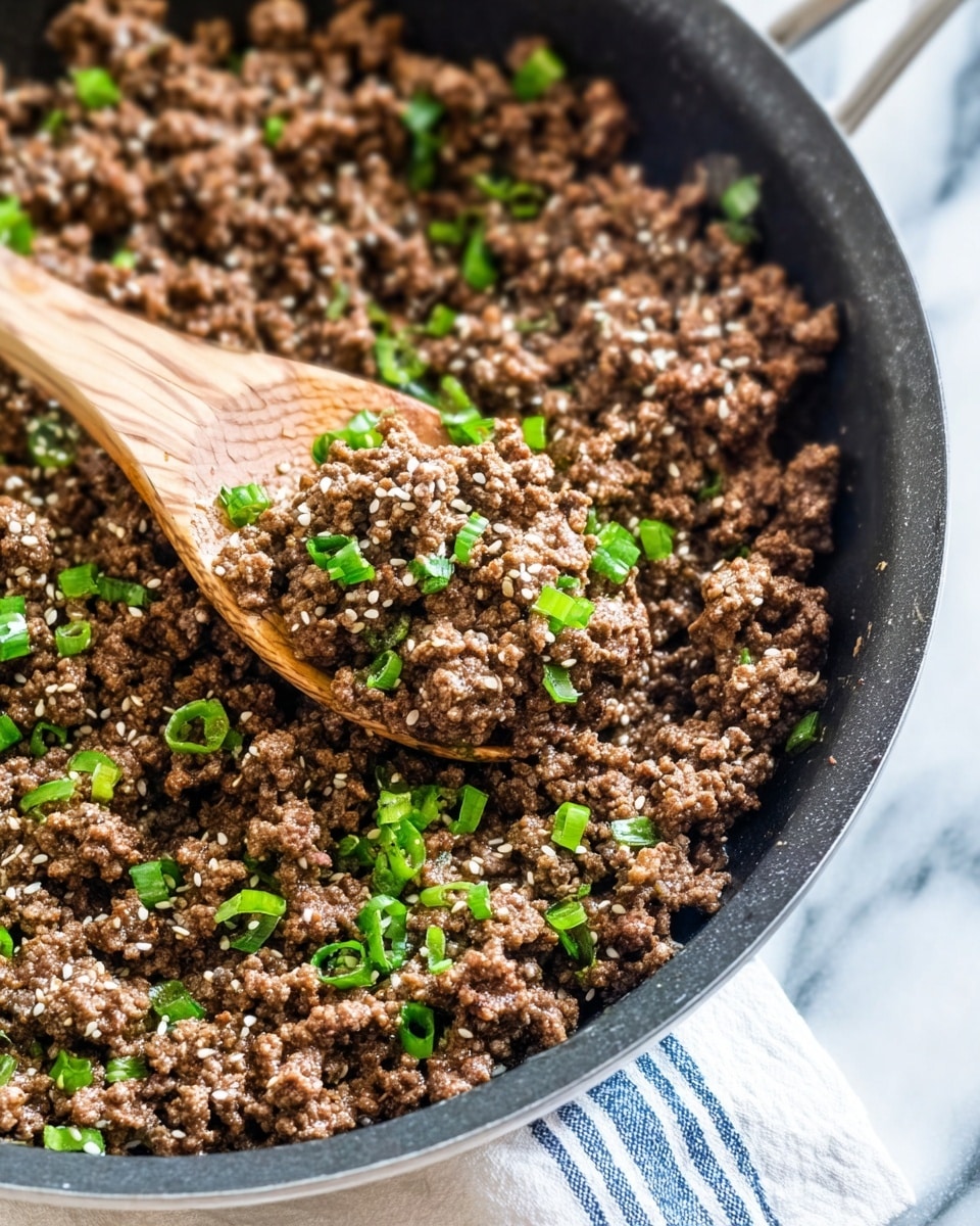 A close-up view of a black skillet filled with cooked ground beef mixed with small green onion pieces and sprinkled with white sesame seeds. The beef is brown and crumbly with a saucy texture that looks moist. A wooden spoon is lifting a scoop of the beef mixture, showing the texture clearly against the rest of the pan’s contents. The skillet rests on a white marbled surface with a checkered cloth partially visible nearby. photo taken with an iphone --ar 4:5 --v 7