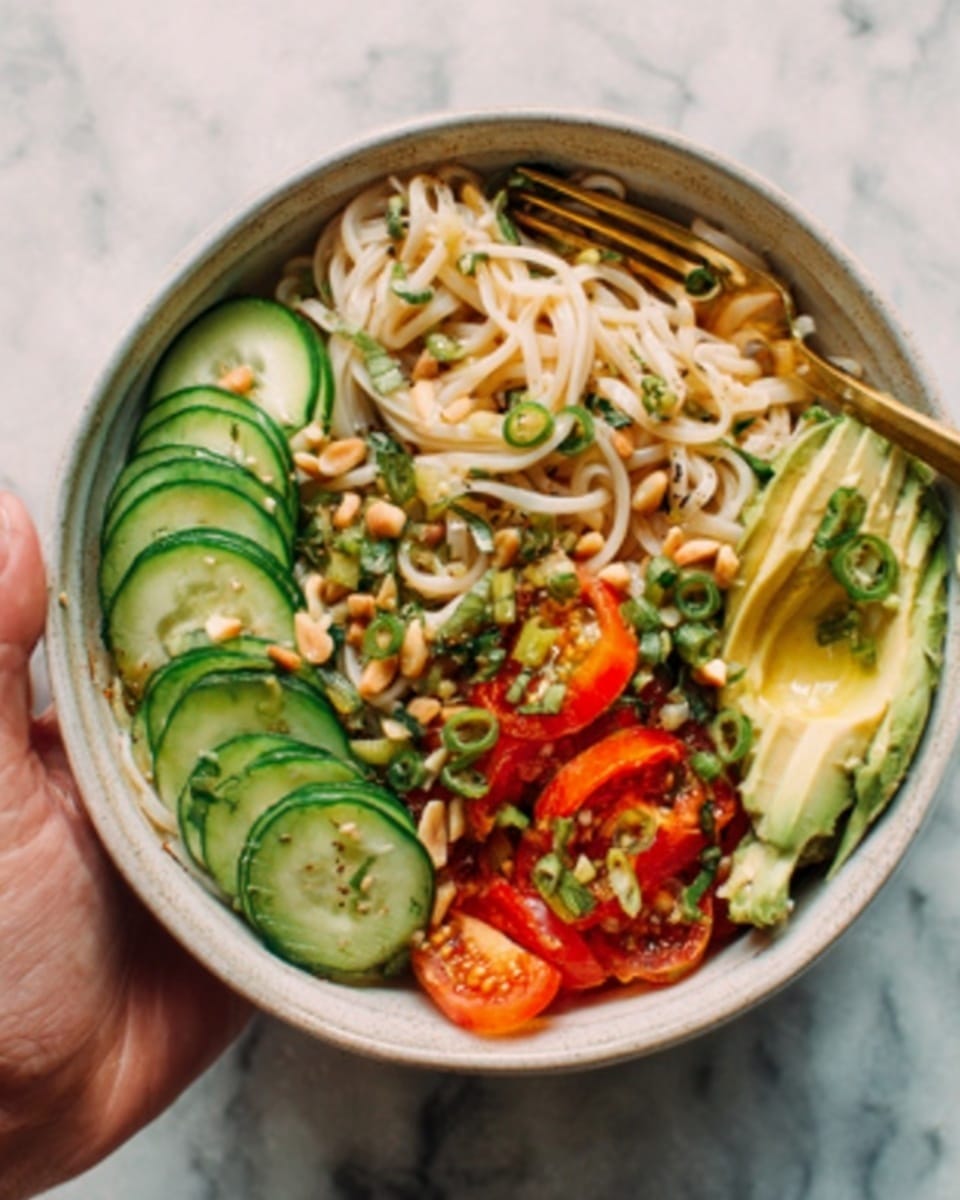A white bowl holds a colorful noodle salad with several layers: at the bottom, light brown noodles with smooth texture; on top, thinly sliced bright green cucumbers arranged in a half-circle; beside them, pale yellow avocado slices fanning out; scattered around are toasted pine nuts and shredded orange carrot strips, adding crunch and color; a woman's hand is about to pick up some with wooden chopsticks; the bowl sits on a white marbled surface. Photo taken with an iphone --ar 4:5 --v 7