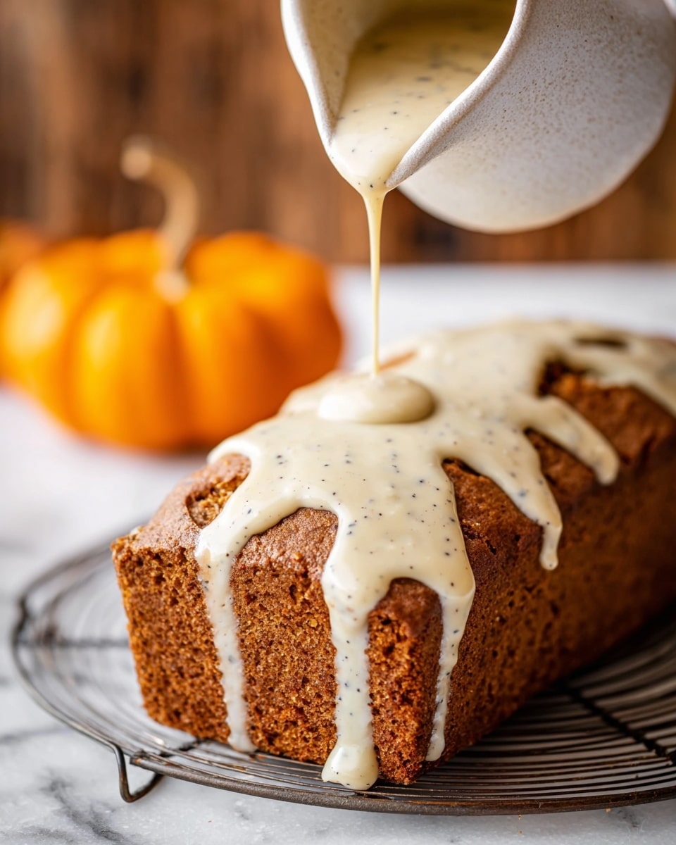 A golden-brown loaf cake with a rough, textured crust sits on a round white marbled surface. A white ceramic pitcher delicately pours a thick, creamy pale beige glaze flecked with small dark specks over the top of the cake, causing the glaze to drip unevenly down the sides. In the blurred background, an orange pumpkin adds a touch of color. The image captures the moment the glaze lands, highlighting the contrast between the warm cake and smooth topping. Photo taken with an iphone --ar 4:5 --v 7