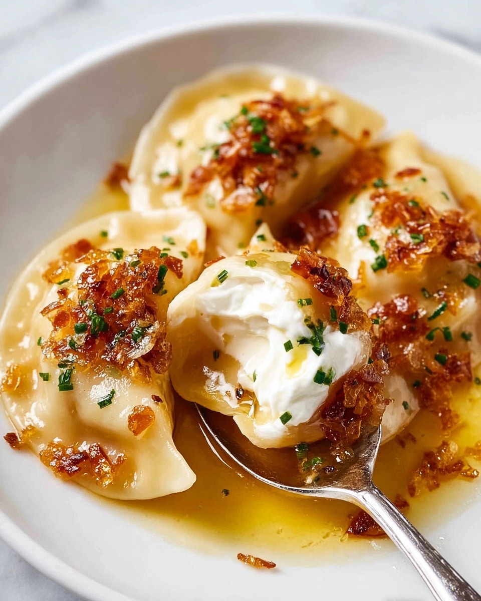 The image shows a white plate with two large pierogies, each with a light golden, slightly translucent dough. The pierogies are topped with caramelized finely chopped onions that are a deep golden-brown color, scattered evenly over and around the dumplings. One pierogi is held on a silver spoon, lifted slightly above the plate, and has a dollop of white sour cream on top with a small drizzle of golden oil. Small green parsley pieces are sprinkled on the pierogies and sauce, adding a fresh touch. The plate sits on a white marbled surface. photo taken with an iphone --ar 4:5 --v 7