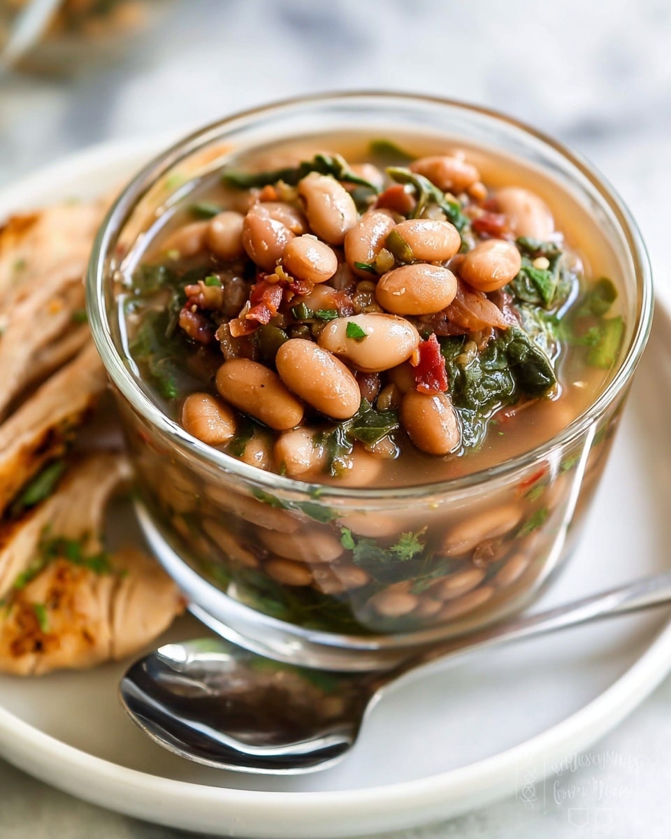 The image shows a clear glass bowl filled with pinto beans mixed with greens and small pieces of vegetables, all sitting in a light brown broth. The bowl is placed on a white plate, and a silver spoon rests on the plate next to the bowl. The beans are the top layer, visibly whole and shiny, with bits of green herbs and red pieces mixed in. Around the bowl on the plate are strips of cooked chicken with a slight brown seasoning. The background and surface show a white marbled texture, giving a clean and fresh look. Photo taken with an iphone --ar 4:5 --v 7