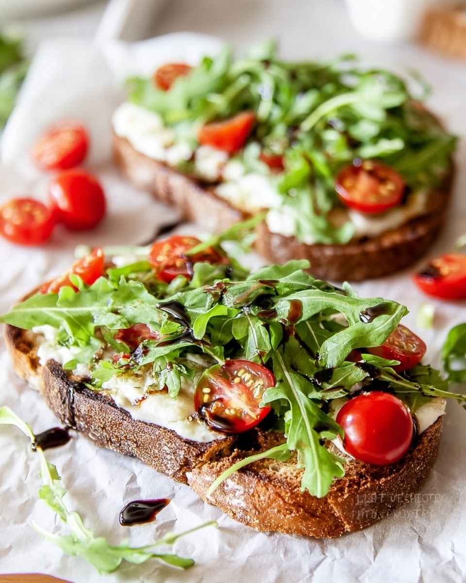 Two open-faced sandwiches are shown on crinkled white parchment paper over a white marbled surface. Each sandwich has one slice of toasted, dark brown crusty bread as the bottom layer. A spread of white cheese or cream covers the bread. Fresh bright green arugula leaves are scattered on top, with halved cherry tomatoes of vivid red resting over the greens. There are some dark balsamic glaze drizzles adding contrast across the arugula and tomatoes. The texture is fresh and vibrant with a mix of soft cheese, crunchy bread, and crisp vegetables. photo taken with an iphone --ar 4:5 --v 7
