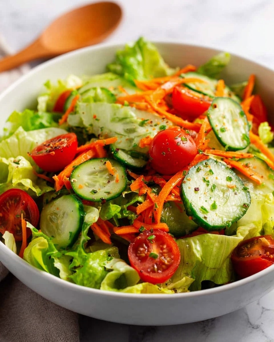 A white bowl filled with a fresh mixed salad featuring three main visible layers: a base layer of light green, crisp lettuce leaves, followed by a middle layer of thin, bright orange shredded carrots spread evenly, and a top layer of sliced dark green cucumbers with pale centers and small, shiny red cherry tomatoes scattered on top. The vegetables have a light sprinkle of black pepper or seasoning, with the textures showing the crunchiness of the greens and the smoothness of the cucumbers and tomatoes. A wooden spoon is placed inside the bowl on the left side, with the bowl set on a white marbled surface photo taken with an iphone --ar 4:5 --v 7