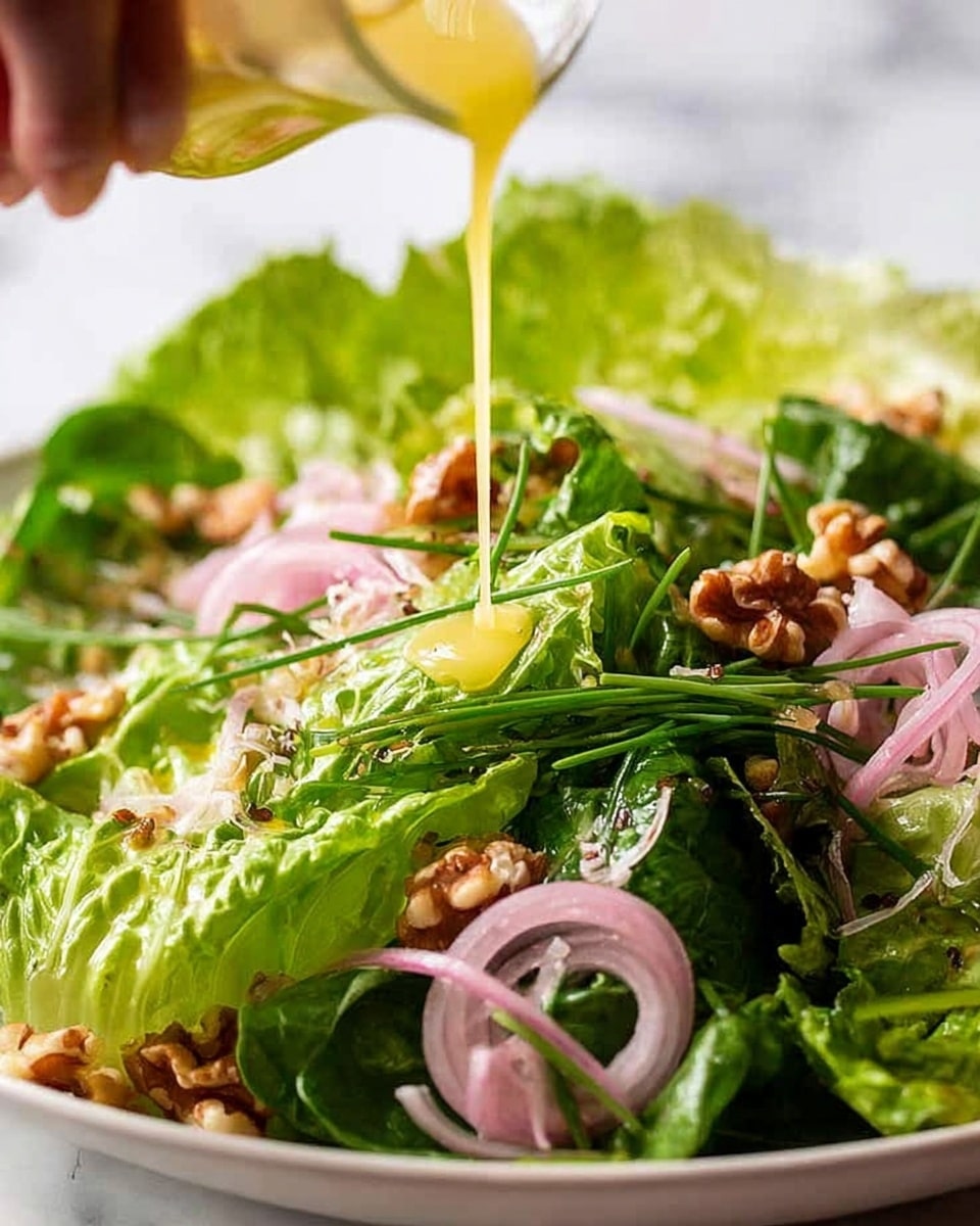 A close-up image of a fresh green salad on a white bowl sitting on a white marbled surface. The salad has multiple layers starting with bright green lettuce leaves forming the base, scattered with light pink thinly sliced onion rings, and dark green chives laying across. On top, there are rough-textured brown walnut pieces evenly spread. A woman's hand is pouring a yellow dressing over the salad, creating a glossy wet look on the leaves and walnuts. photo taken with an iphone --ar 4:5 --v 7