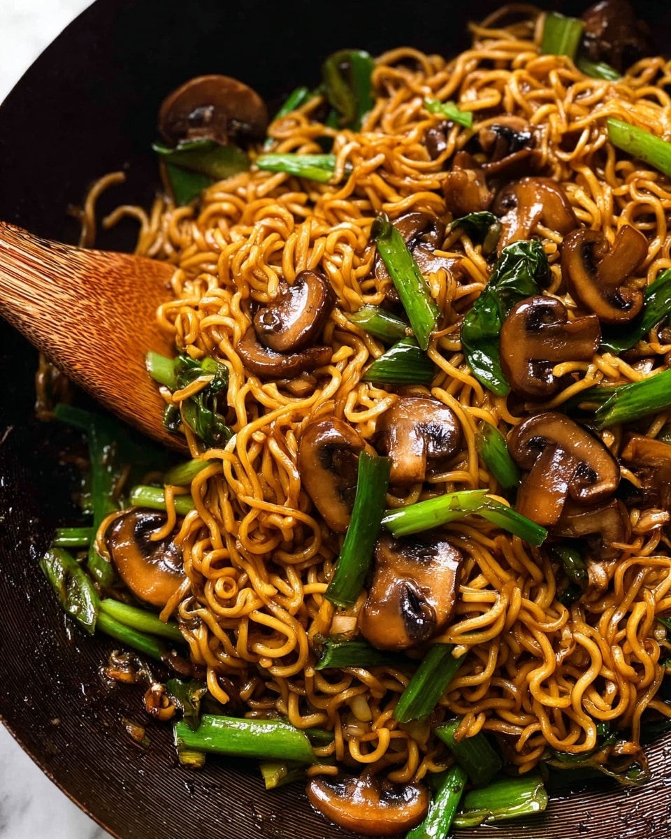 Close-up of cooked noodles mixed with sliced brown mushrooms and bright green scallions. The noodles are shiny and brown from sauce, with a slightly curly texture. The mushrooms are scattered evenly, showing a smooth, moist surface, while the scallions add fresh green pops throughout. A wooden spatula is partially visible, stirring the noodles. The dish sits on a white marbled texture background. photo taken with an iphone --ar 4:5 --v 7