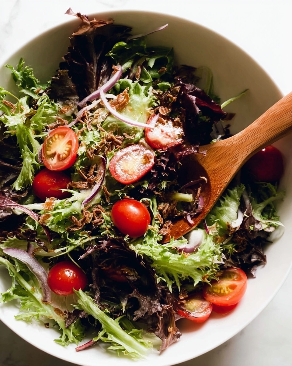 A white bowl filled with a fresh salad showing about three layers: the first layer is a mix of dark and light green leafy lettuce with curly edges, the second layer includes bright red cherry tomatoes, some whole and some sliced in half, and thin slices of pale purple onion, and the top layer is sprinkled with small, light brown crispy bits scattered unevenly. A wooden spoon is partially buried in the salad on the right side. The bowl sits on a white marbled surface. photo taken with an iphone --ar 4:5 --v 7